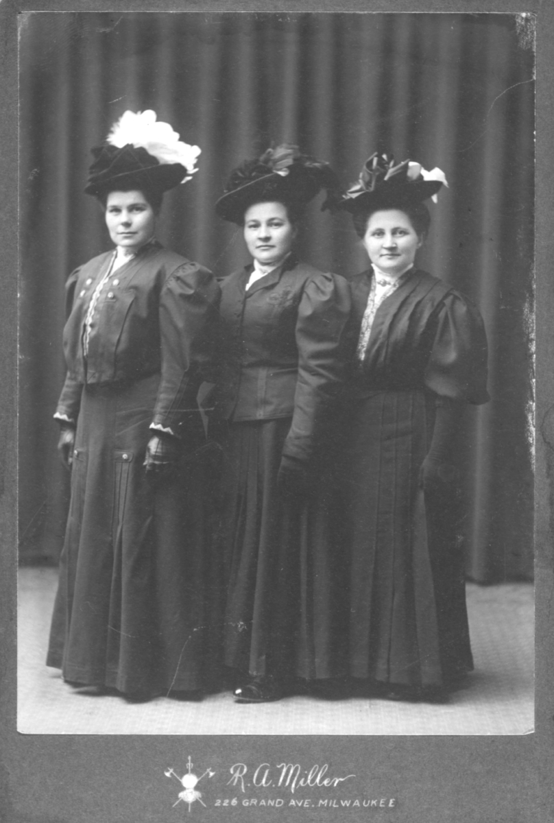 Fra venstre: Nanna Korbi, søsteren Elmine Eugenie Korbi og Hilma Mikkelsen Halonen, alle fra Vadsø. De har på seg mørke kjoler, store hatter og hansker. Bildet er trolig tatt i Milwaukee, USA. Kvinnene på bildet er Amerika-emigranter fra Vadsø, Nord-Varanger.