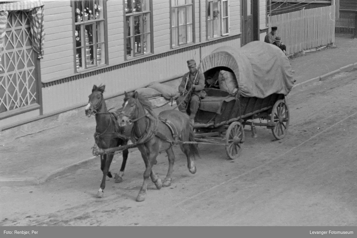 Tysk soldat kjører forsyninger med hest, bygningen bak sikret.