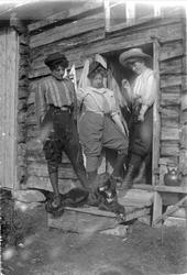 Tre kvinner poserer i en døråpningen til et tømmerhus, iført