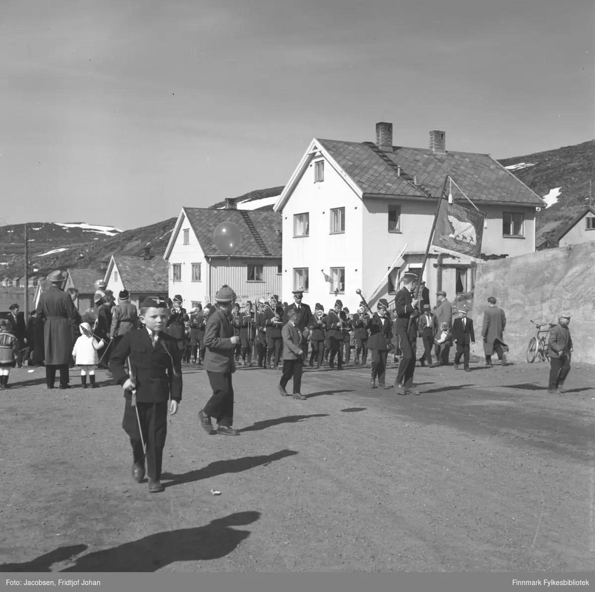 17. mai-feiring i Hammerfest. Bildet viser et musikk-korps og flere festkledt mennesker i Skolebakken. Huset til høyre på bildet tilhørte Alf Paulsen som var dirigent for skolekorpset.