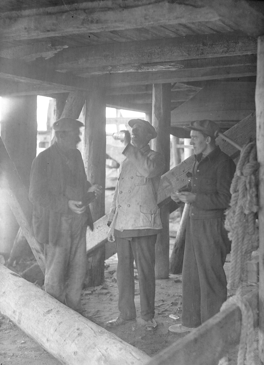 Tre menn drikker brennevin under ei brygge