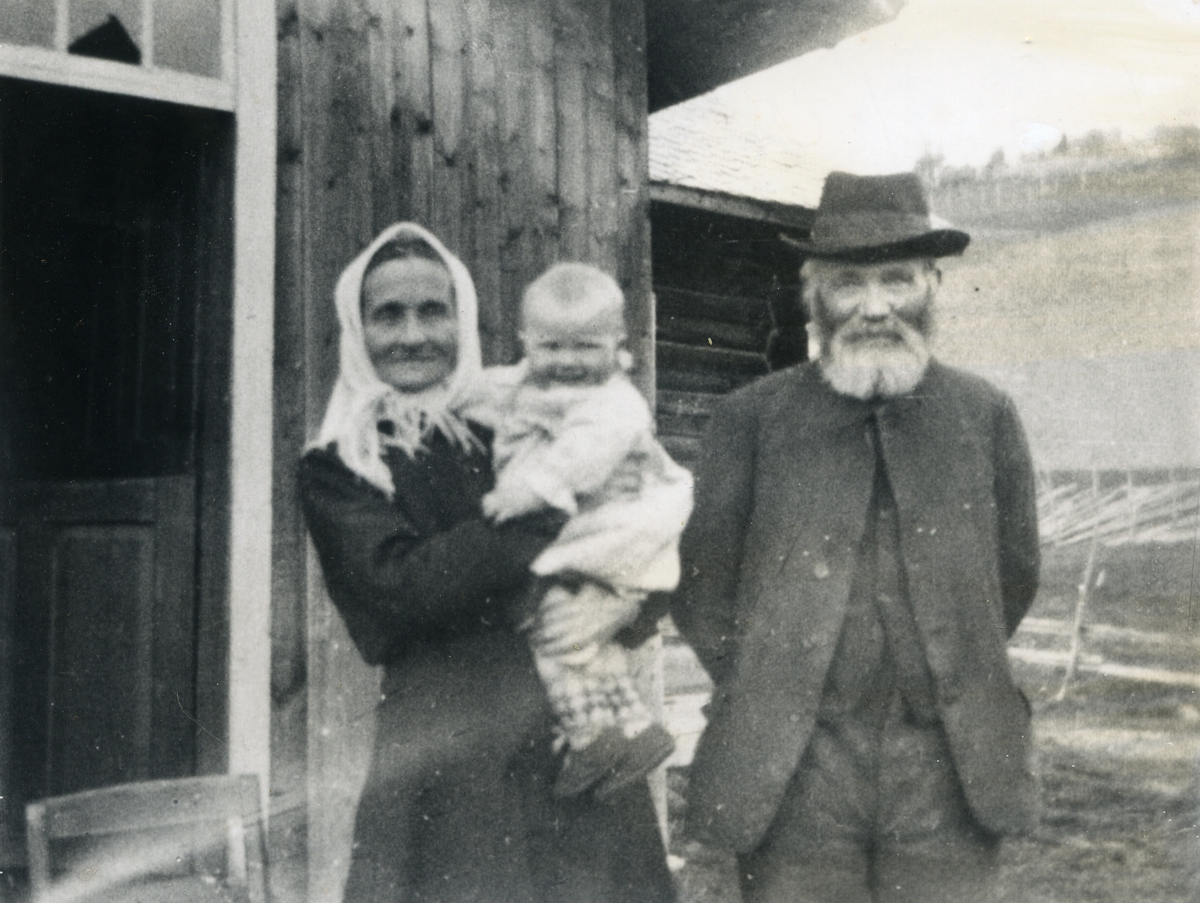 Eldre mann og kvinne framfor bygning, ho med eit born på armen. Livaursfolket i Nørre Haugen i Skrautvål