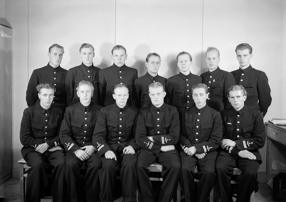 Elever vid furirskolan på F 3 Östgöta flygflottilj, 1942-1943. 13 stycken elever, från F 5 och F 11. Grupporträtt inomhus.