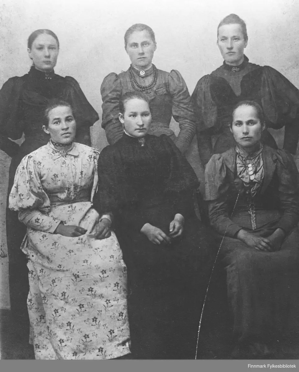 6 unge kvinner hos fotografen. Tre av dem sitter og tre står bak de første. Overste rekke fra venstre: Nanna Evida Birgitte Wara (f.Palo /Ballo), Emilie Wanhaiemi (gift Nilsen), ... Lakkala (f.BerÃ¤vaara) og nederste rekke: Laura Niemi (f.BerÃ¤vaara), de to siste er ukjente. Alle er kledd i lange kjoler og har en smygge rund halsen.
