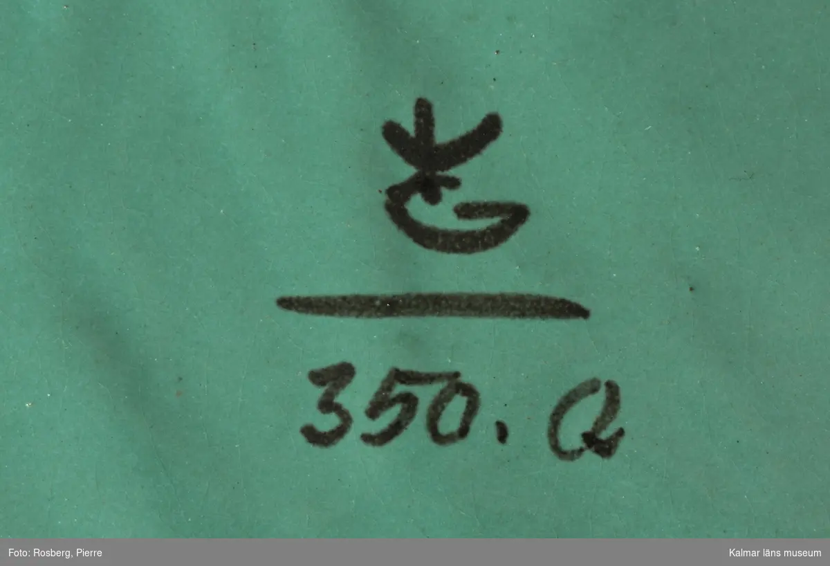 KLM 43946 Askfat av keramik, lergods, grön glasyr.  Åttkantig form, med egyptiska motiv i de åtta fälten rund om, bl a pyramiderna. Målad signatur: krönt G, (började användas 1925), därunder 350. Q. Tillverkad av Gabrielverken. Datering, troligen 1940-tal, glasyren förefaller vara av ett enklare slag som gjordes under andra världskriget, under kriget fick Gabrielverken inte hem glasyrer som tidigare utan man fick göra egna.