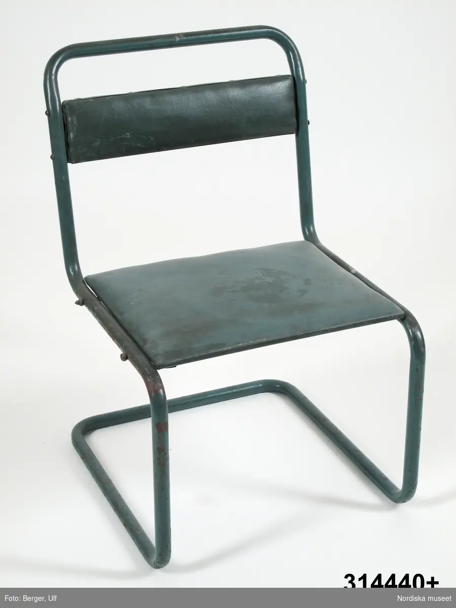Katalogkort:
"Stolarna tillverkade av grönlackerat stålrör med hård stoppning i rygg och sits klädd med grön vaxduk."