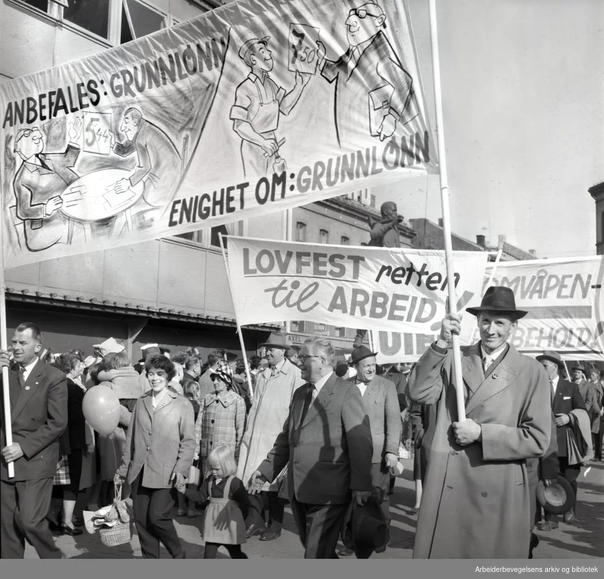 1. mai 1961, kommunistpartiets demonstrasjonstog på Youngstorget. Parole: Anbefales: Grunnlønn. Enighet om: Grunnlønn.Parole: Lovfest retten til arbeid.