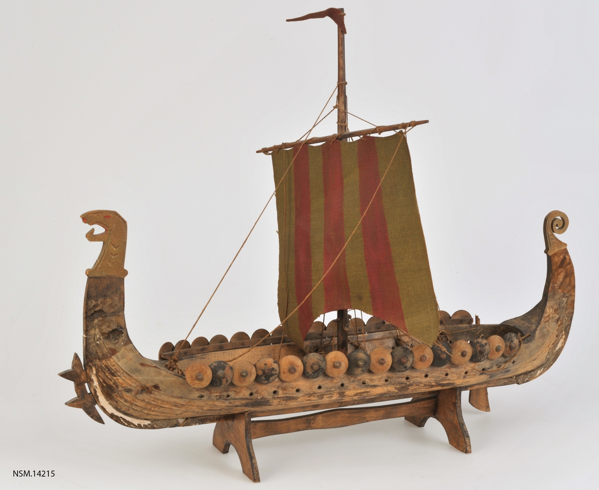 Vikingskip , uthult trestykke (noe grov utførelse), mast, seil med røde og grønne striper, 16 skjold på hver side.