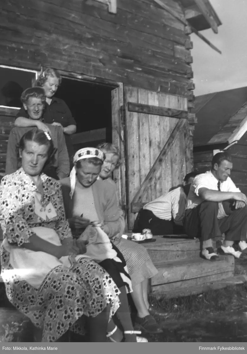 Kaffe på trammen til melkebua på Mikkelsnes, ca. 1950. Sittende, fra venstre: Astrid, Marine og Gudrun Mikkola, Sverre Olsen Lie. Marine broderer. En ukjent mann sitter med ansiktet skjult. Stående bak: Mikkel og Herlaug Mikkola