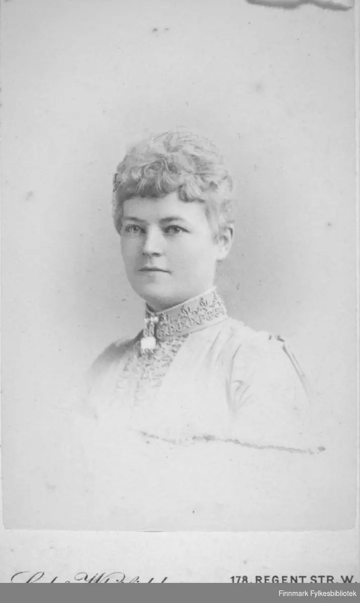 Portrett av en dame iført en lys bluse eller jakke. Den har høy krage med mønster og noe pynt er festet foran i halsen på den.