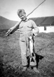 En gutt står med en hjemmelaget, lang fiskestang over skulde