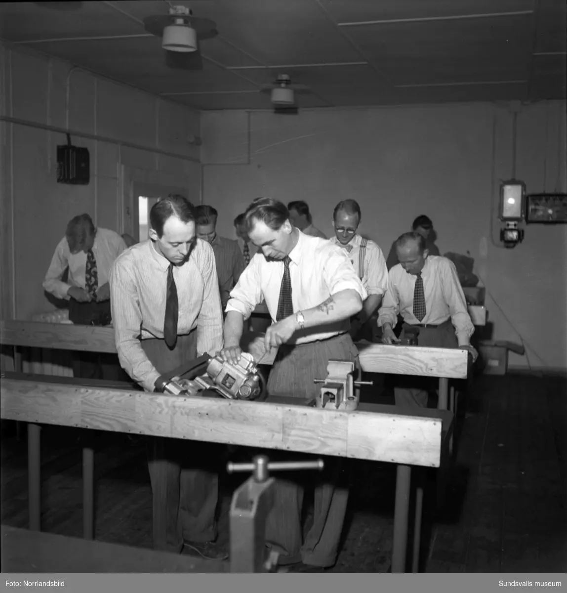 Omskolningsarbete på Verkstadsskolan. Män i skjorta och slips mekar med maskiner.