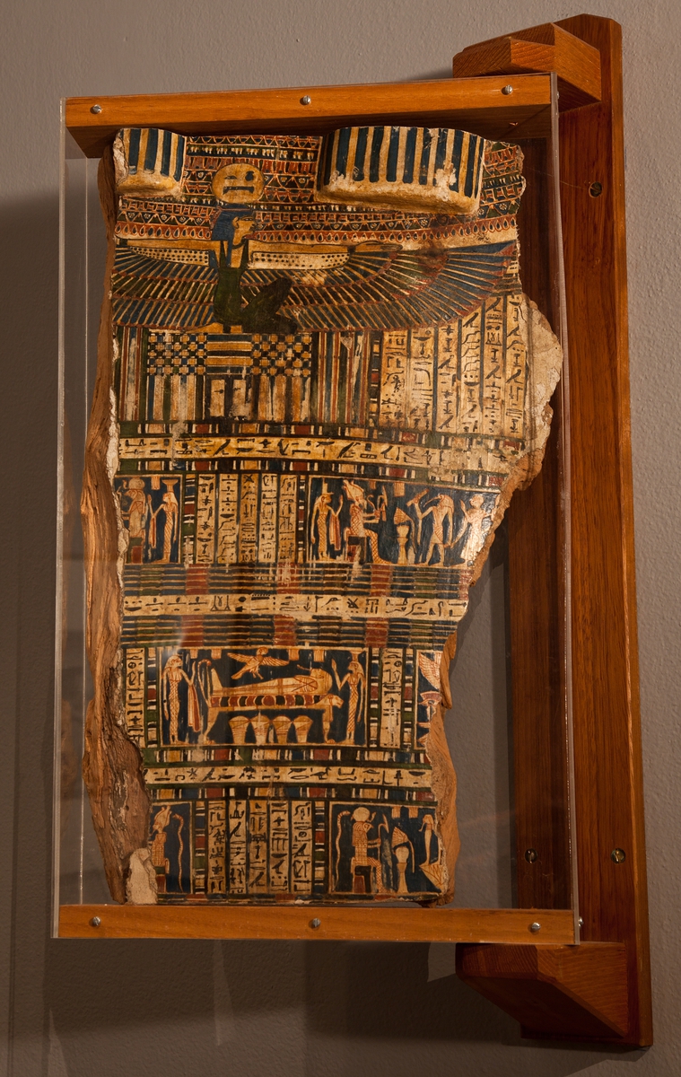 Del av mumiekista. Kistan har en gång rymt mumien efter general Kerserti, 500-talet f.Kr. General Kerserti omnämns i Herodotos reseberättelse från ca 450 f.Kr.

Upphöjningarna överst på kiststycket är nederdelen av peruken. Därunder sitter himmelens gudinna Nut, enligt inskription i soldisken, med bevingade armar. Under henne ses en dörr med lås gravkammarens dörr. Texterna innehåller böner.

Scenen överst till vänster visar den sittande solguden Horus. Bakom honom står gudinnan Neftys. På den högra scenen ses dödsrikets härskare Osiris i mumiegestalt, sittande på en tron, med sin gemål Isis strax bakom sig. Osiris var den gud som skulle döma den döde. Thot, skrivkonstens gud med ibishuvud, håller en papyrusrulle med den dödes gärningar. Bakom honom ses den döde, som leds fram av Thot.

På mittscenen ses den döde liggande på en balsameringssäng, formad som ett lejon. Ovanför den döde ses Ba, en av den dödes själsaspekter, här i form av en fågel. Ba återvänder till kroppen efter balsameringen, men kan också förflytta sig obehindrat mellan olika världar. Under balsameringssängen står fyra urnor, så kallade kanoper. De innehåller den dödes inre organ, vilka togs ur kroppen vid balsameringen. Kvinnan till vänster är Isis och den till höger Neftys, vilka skyddar den döde.

Den nedre scenen till vänster visar Osiris sittande på en tron. Scenen till höger visar Horus, solguden, som skulle visa den rätta vägen väster ut till de dödas värld. Framför honom syns en av de fyra Horus-sönerna som hade till uppgift att skydda den dödes inälvor.
