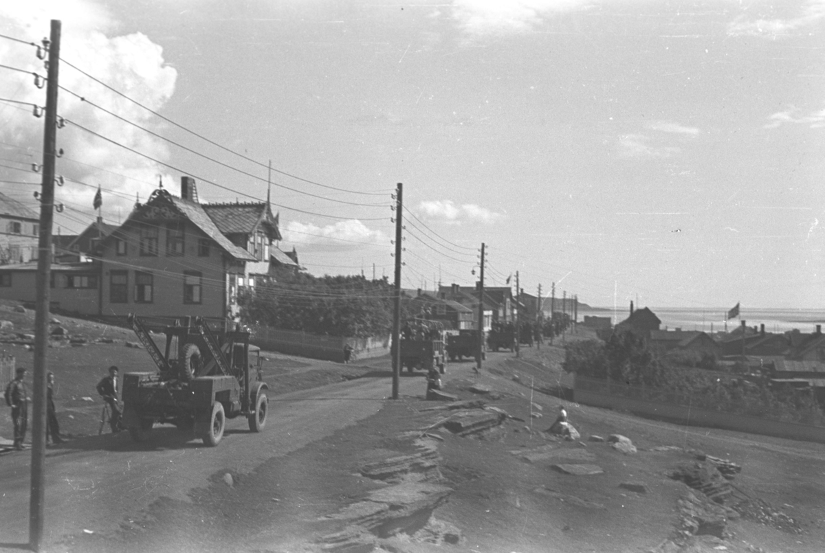 En kolonne med lastebiler og anleggsmaskiner kjører nedover en gate i Vadsø.
