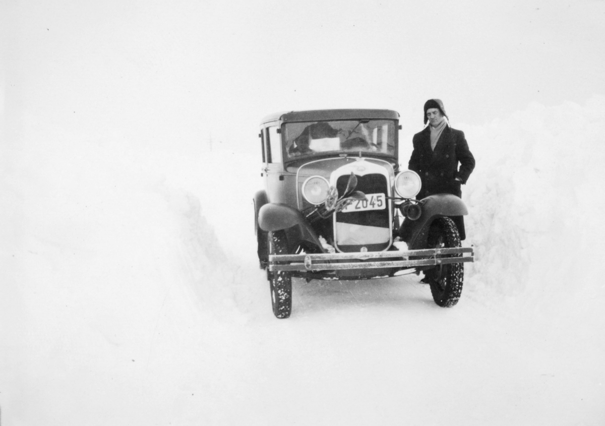 En mann står ved siden av en Ford A-modell fra 1930. Det er vinter og sne. Mannen er kledt i frakk . Han har lue og skjerf på seg. Bilnummeret er Y2045.  I Norges Bilbok 1935 står nummeret registrert på drosjeeier Georg S. Dahl i Vadsø.