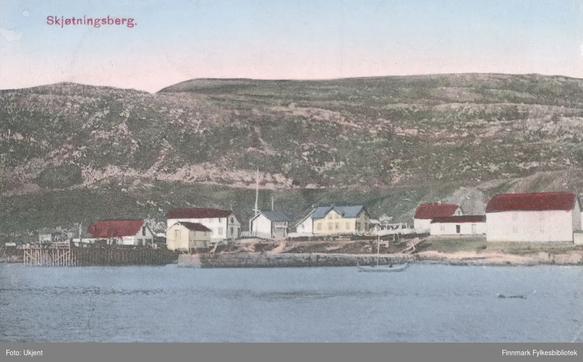 Et postkort med Skjøtningsberg som motiv. På bildet kan man se en havn med kai, båter, en mollo(?) og bygninger. I bakgrunnen kan man se fjell.