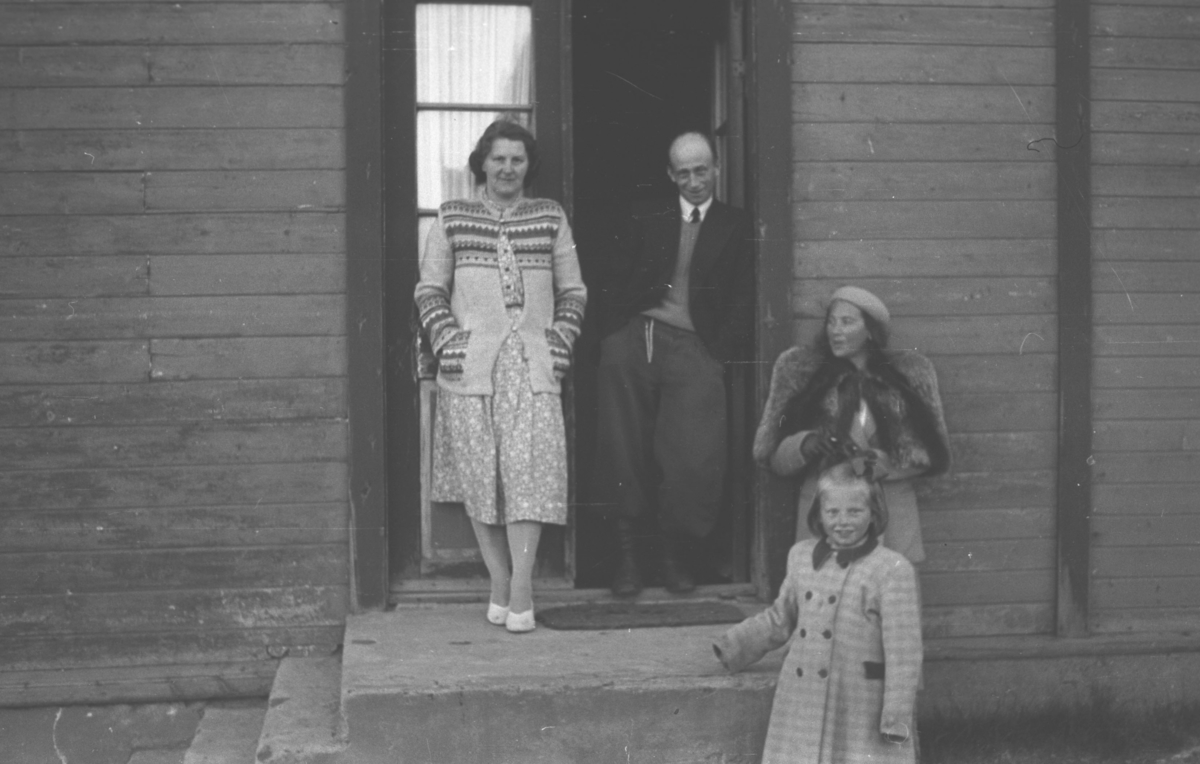 Fire personer står ved en inngangsparti til en bolig. Fra venstre: Rønnaug Haldorsen, Saralf Haldorsen, Frida Hauge, og foran Frida er Erna (Tulla) Haldorsen. Bildet er tatt i Vadsø på trappa til boligen der familien Haldorsen bodde. 