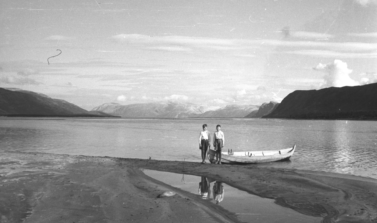 Øystein og Rolf Hauge ved bredden av Tana-elva med en elvebåt liggende rett bak dem.