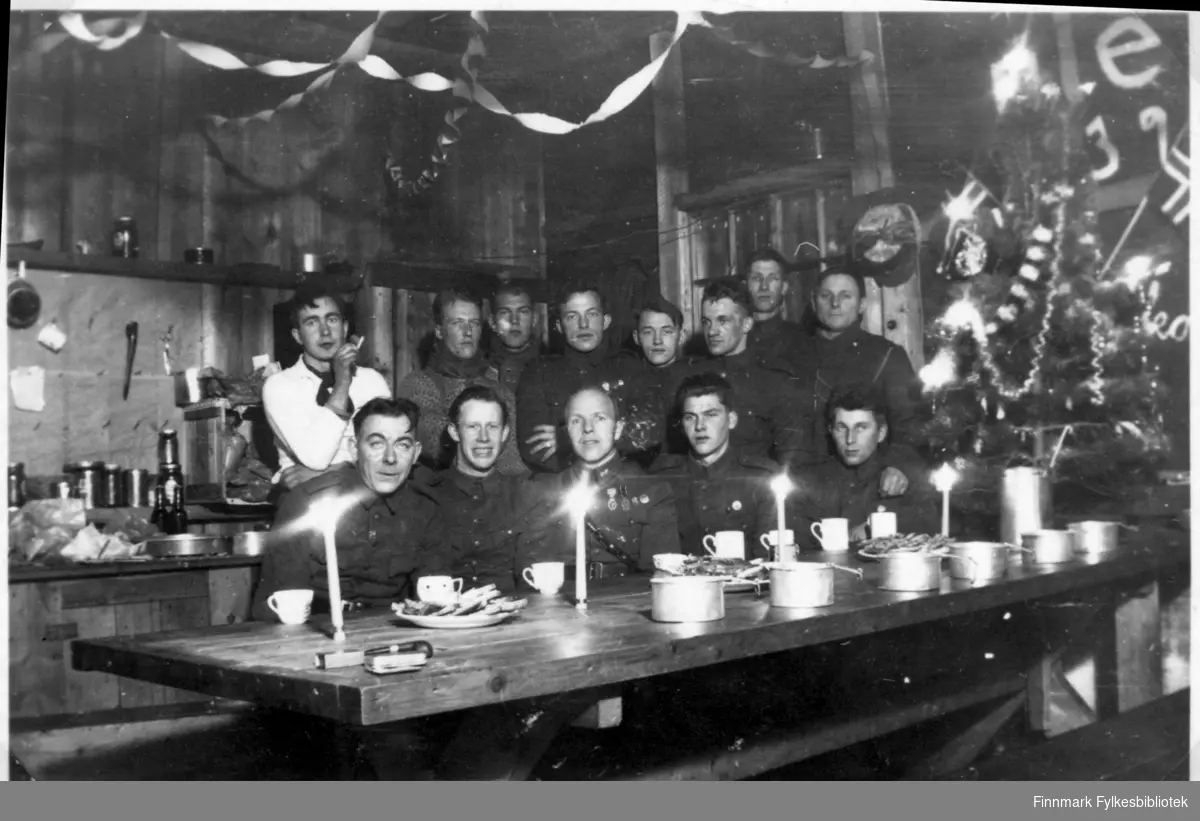 Garnisonen i Sør-Varanger. Gruppebilde fotografert inne i brakka, fra messa. Middag, stearinlys, julefeiring julepynt, feststemning. Soldatene samlet til fotografering