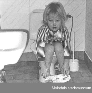 Ett barn sitter på toaletten i väntan på hjälp. Bild tagen till Mölndals museums utställning 1993 om och av daghemmet.