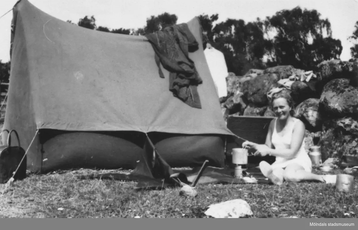 Rosa Pettersson kokar gröt på ett bensinkök under en tältsemester någonstans i Dalarna 1957. Familjen hade skaffat en begagnad bil (Opel Olympia av 1949 års modell) och under somrarna reste de till olika landskap i Sverige. Tältet var lånat.