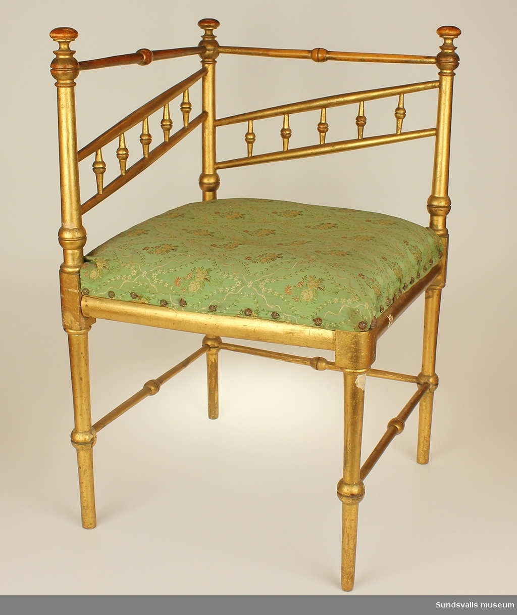 En guldkolorerad svarvad björkstol. Sits av sadelgjord och tagelfylld dyna som klätts med vit och rödblommigt grönt möbeltyg vilket fastsatts med möbelspik i form av stiliserade prästkragar. Nr 1 av ett par.