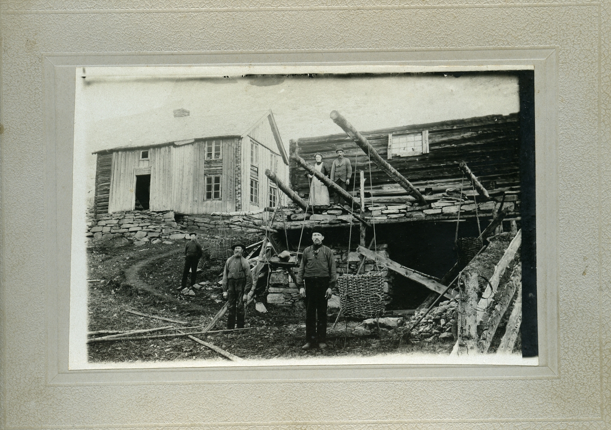 Bildet viser en gruppe mennesker foran trehusbebyggelse. Mulige arbeidsfolk som kan stå foran sitt arbeid.