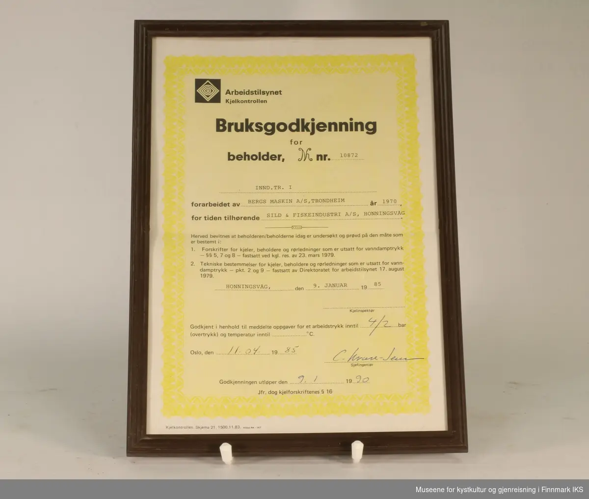 Bruksgodkjenning for INND. TR. I (beholder nr. 10872) hos Sild & Fiskeindustri AS, utsendt av Arbeidstilsynet Kjelkontrollen i 1985. Hvitt og gult papir med sort tekst. Utfylt for hånd. Innrammet.
