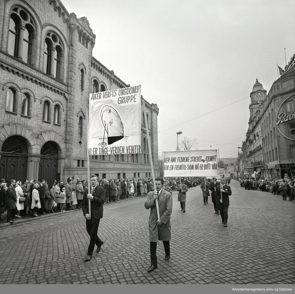 1. mai 1963 i Oslo.Demonstrasjonstoget i Karl Johans gate..Parole: Aker Verfts Ungdomsgruppe.Vi er unge - verden venter.Parole: Her har fedrene strevet og kjempet for en fremtid - som nå er blitt vår