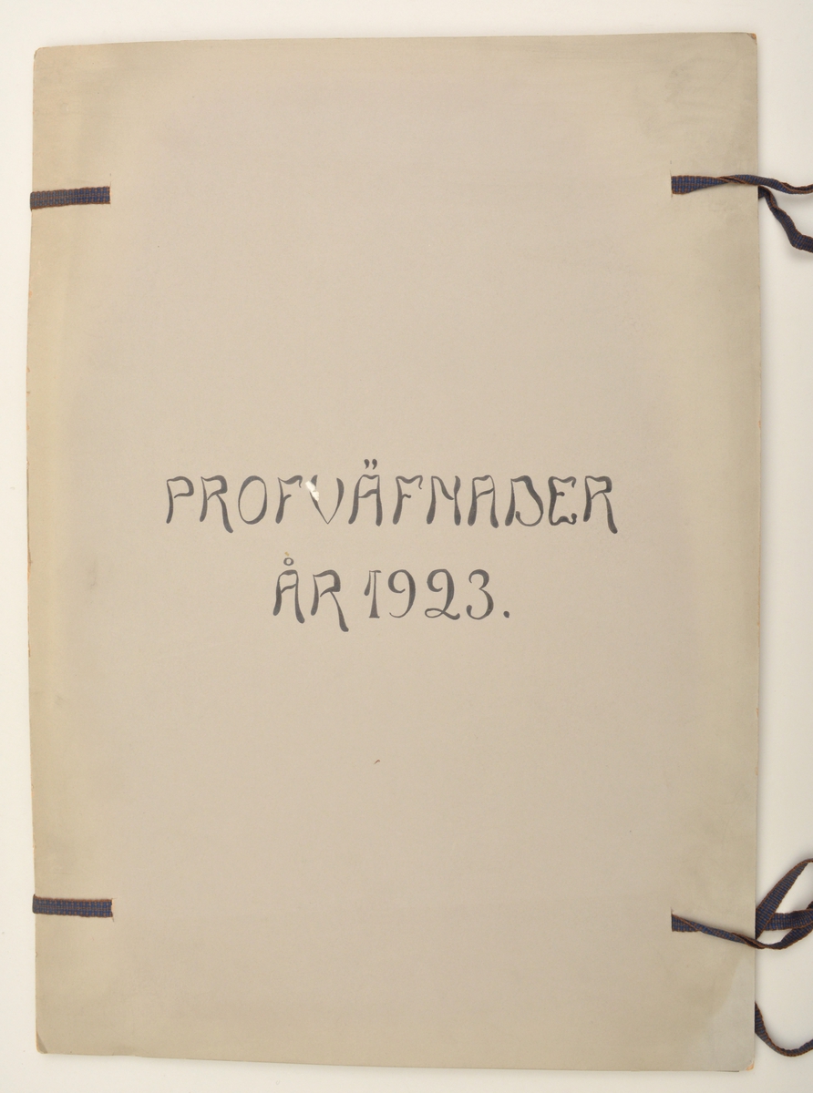 Stor pappersmapp med lösa blad med påklistrade tygprover. Pärmarna är av en annan papperskvalité än papperna innuti. Pärmarna hålls ihop med ett par långa, handvävda band.
Text på framsidan; "Väfprofer År 1923".