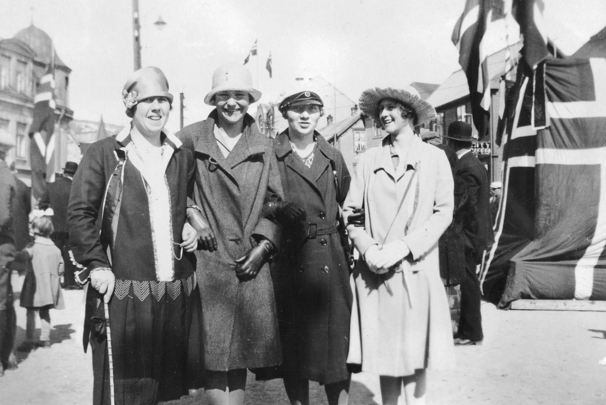 Gruppebilde av fire unge kvinner. Flaggdekorert talerstol bak til høyre.