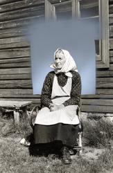 Kvinne som sitter utenfor vinduet i en tømmerbygning. Hun er