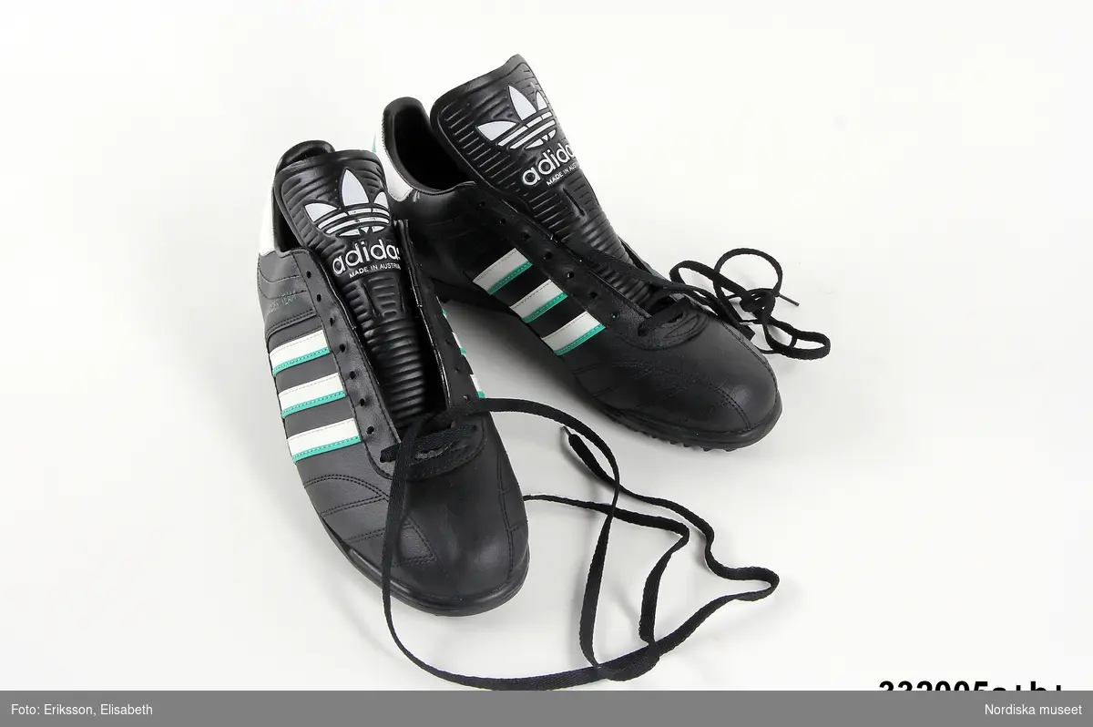 Ett par fotbollsskor. Skorna är svarta med vita och gröna ränder. Adidas logotyp finns på tre ställen på vardera sko. Text på utsidan av skorna: Soccer team. Sko av PVC-plast.  Svarta skosnören av syntet. Storlek 43 1/3. Anm: Oanvända.
/Johanna Skoglund 2013-05-28