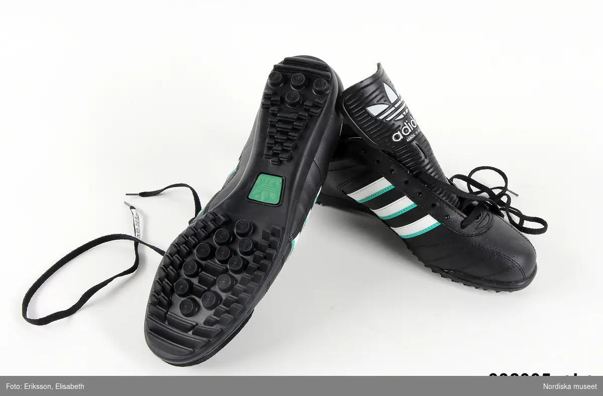 Ett par fotbollsskor. Skorna är svarta med vita och gröna ränder. Adidas logotyp finns på tre ställen på vardera sko. Text på utsidan av skorna: Soccer team. Sko av PVC-plast.  Svarta skosnören av syntet. Storlek 43 1/3. Anm: Oanvända.
/Johanna Skoglund 2013-05-28