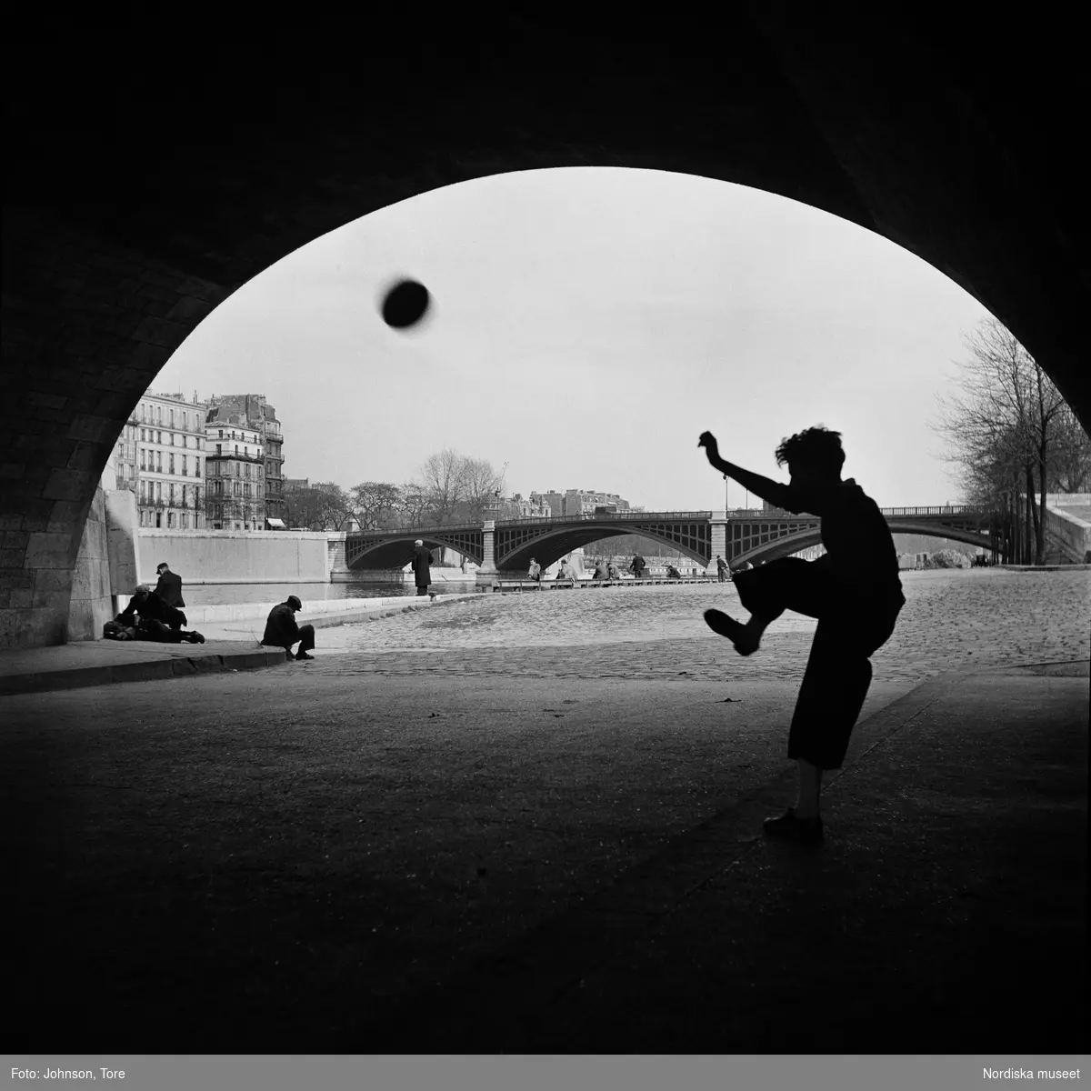 Paris. En pojke sparkar fotboll under en bro.