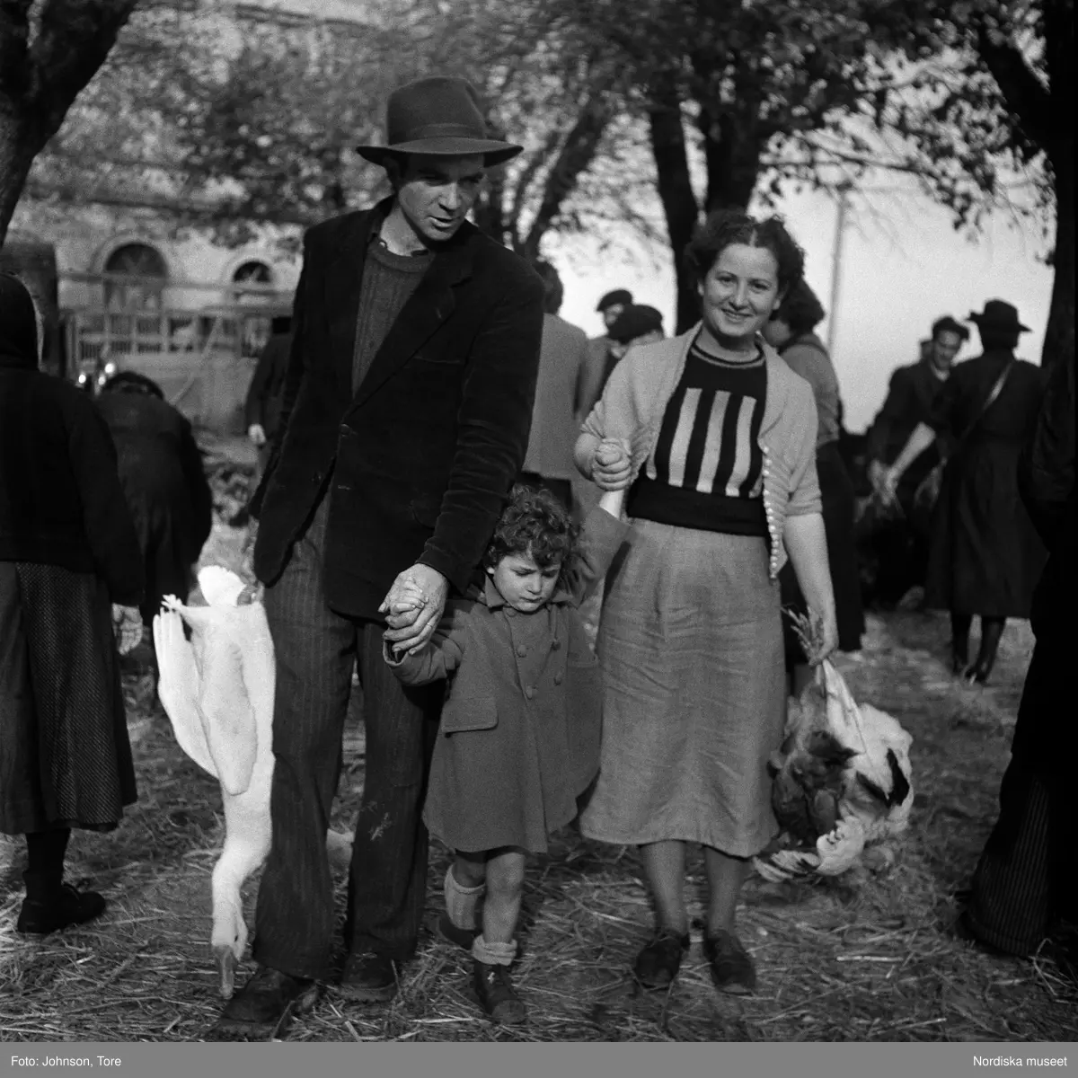 Paris. På väg från marknaden. Föräldrar hållande varsin död fågel, en gås och en höna, sonen i mitten.