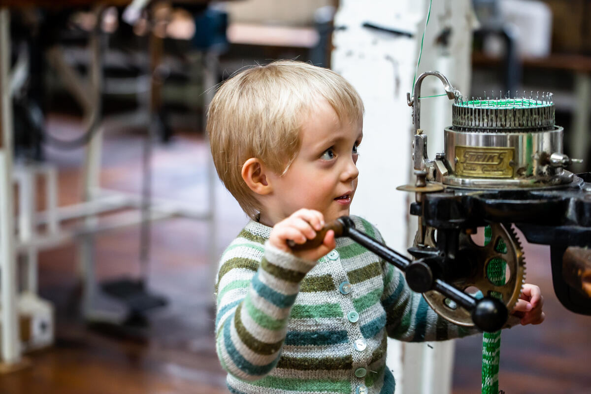 gut med strikkegenser sveivar på strikkemaskin på Tekstilindustrimuseet