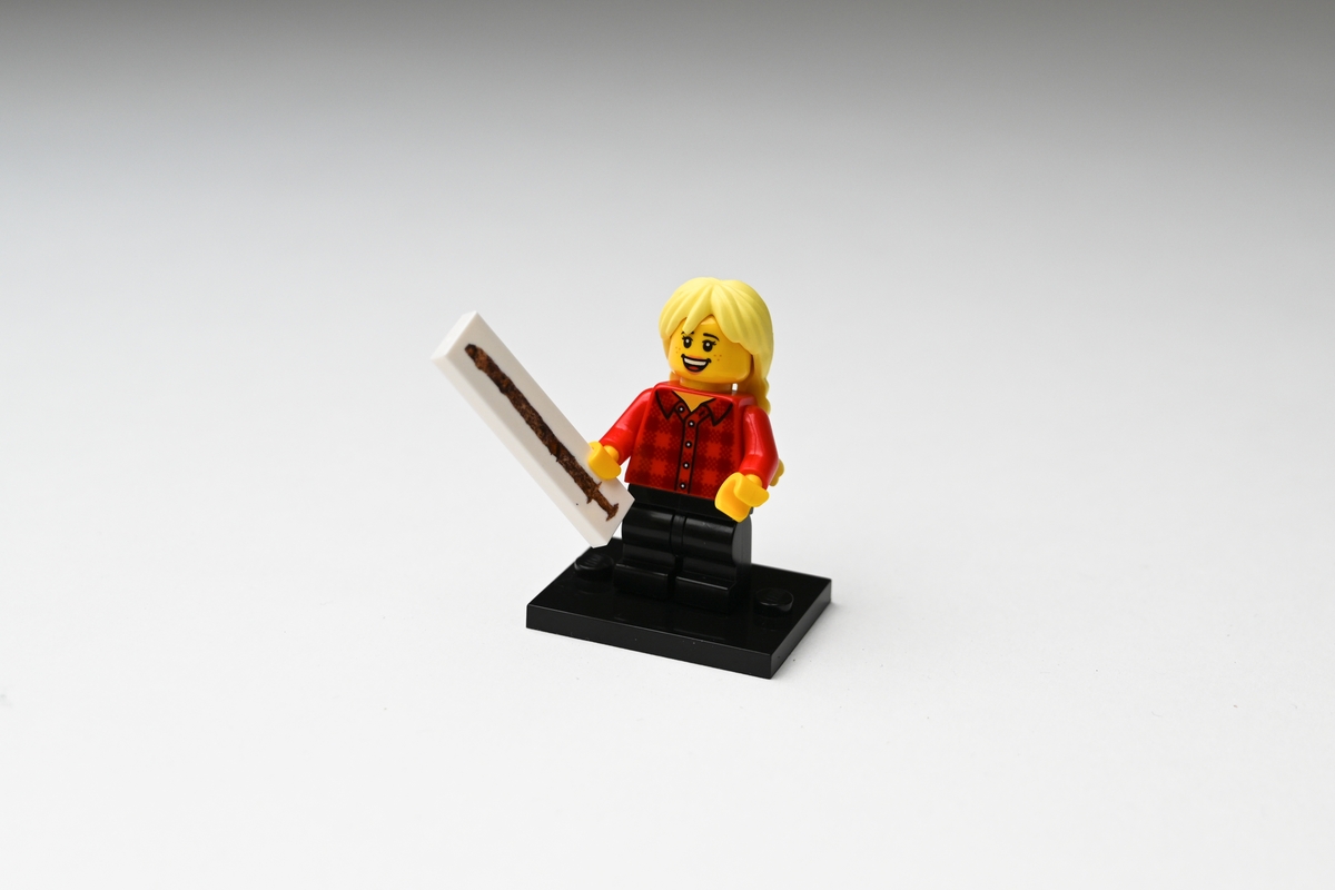 Legofigur av plast föreställande en flicka som håller upp ett svärd i ena handen. Flickan har gult hår i två flätor på ryggen, är klädd i röd- och svartrutig skjorta och svarta byxor. Figuren står på en svart platta. På en vit avlång platta, som figuren håller i handen, finns en bild av svärdsfyndet från Tånnö socken, Jönköpings län. Se vidare Historik.

Figuren förvärvades i en liten plastpåse med fasthäftad pappersetikett.