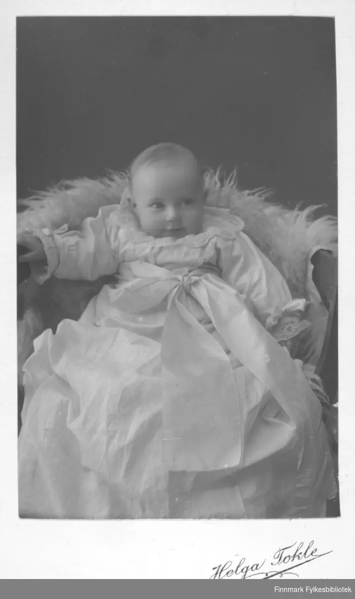 Fotoatelier portrett av baby, muligens fotografert i dåpskjole. Helga Tokle er fotograf, Kirkenes.