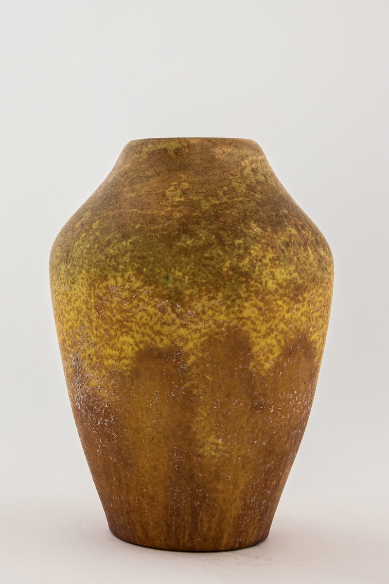 Pæreformet vase av leirgods. Overflaten er dekket av en matt gul- og oransjefarget glasur, tidvis spettet.