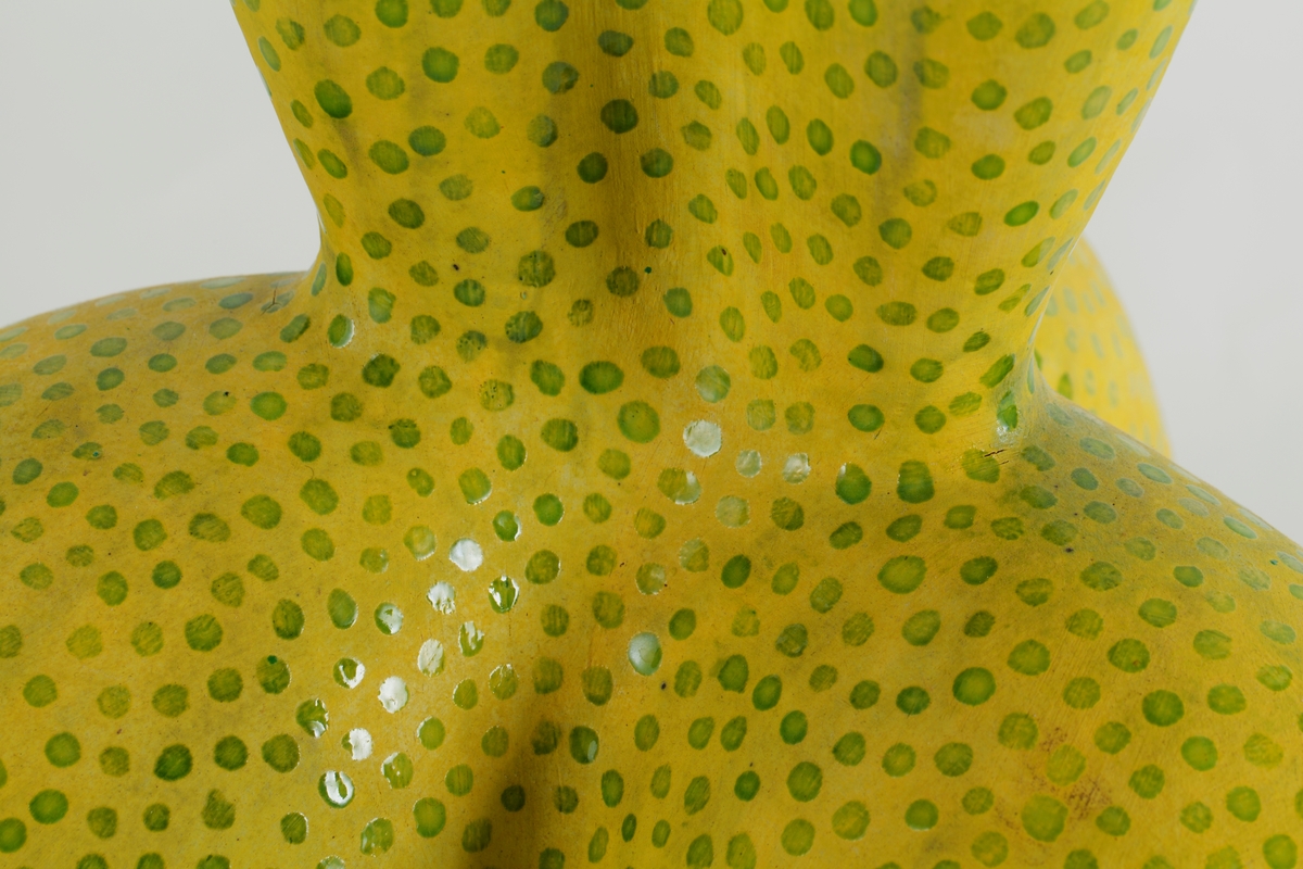 Stor, skulpturell krukke i leirgods. Organisk form som minner om en blomst; nederst tre belgformer, og opp fra denne en svulmende korpus med buede vegger og vid, bølgende munning. Formuttrykket er samtidig kroppslig og vitalt som en muskel. Oransje begitning innvendig, gul med grønne delvis transparente runde glasurflekker utvendig.