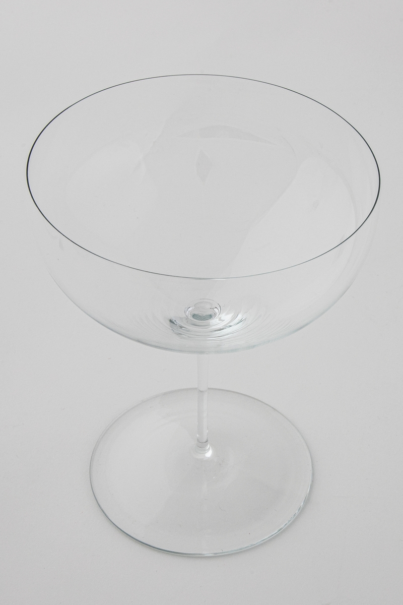 Cognacglass i meget tynt klart glass. Vid kupa som bæres av en meget tynn stett. Sirkulær fotplate, noe hevet på midten.