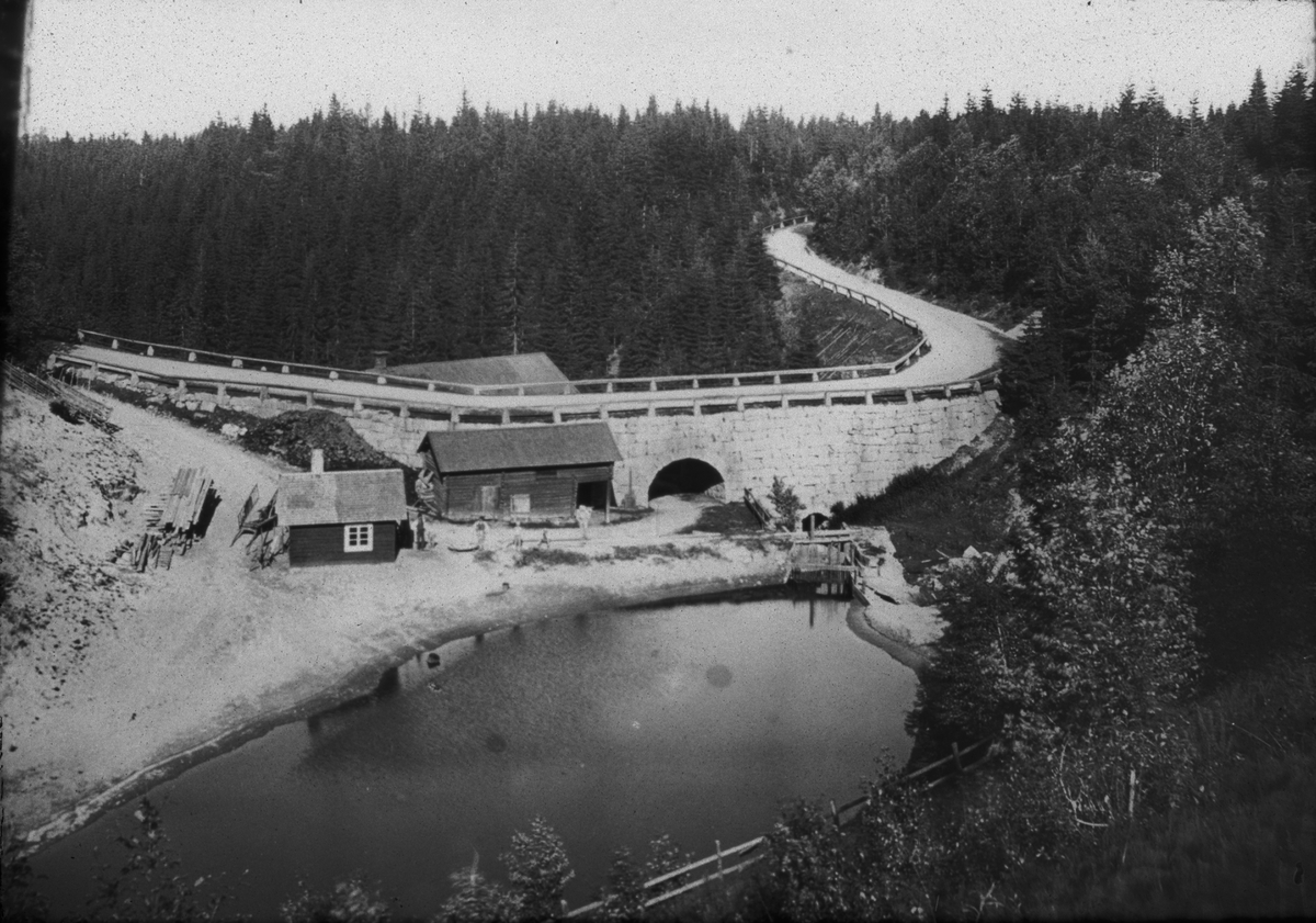 Diapositiv med motiv av väg och viadukt med litet hus framför. Bilden är tagen vid Solvarbo kvarnen, Gustafs socken, Säters kommun. Viadukten byggdes ca 1870.