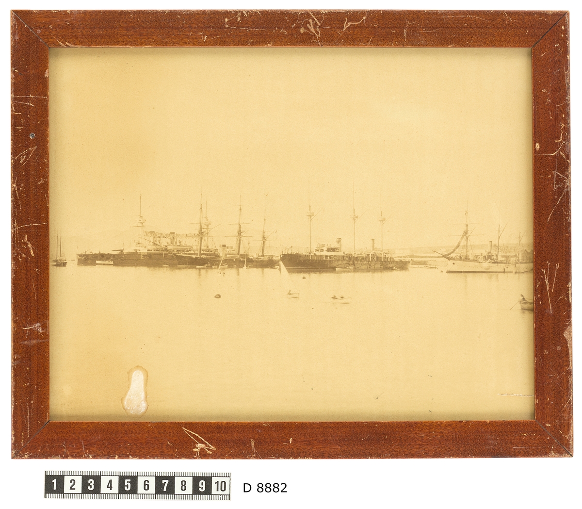 Bilden föreställer ångkorvetten Balder som ligger till ankars i Pireus bredvid tre andra örlogsfartyg. Fartygets syns från babordssidan med bärgade segel. Framför skeppet pågår en livlig trafik med skeppsbåtar.