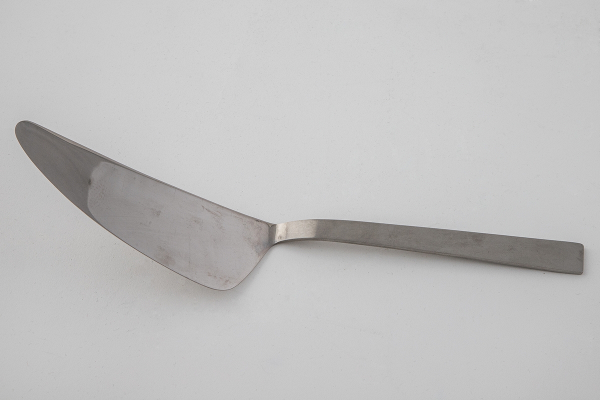 Stor serveringskniv i polert, rustfritt stål. Bladet danner en butt vinkel fra det rettlinjede skaftet. Sistnevnte er mattert, mens bladet er polert, slik at det oppstår en kontrast mellom de blanke og matte partiene