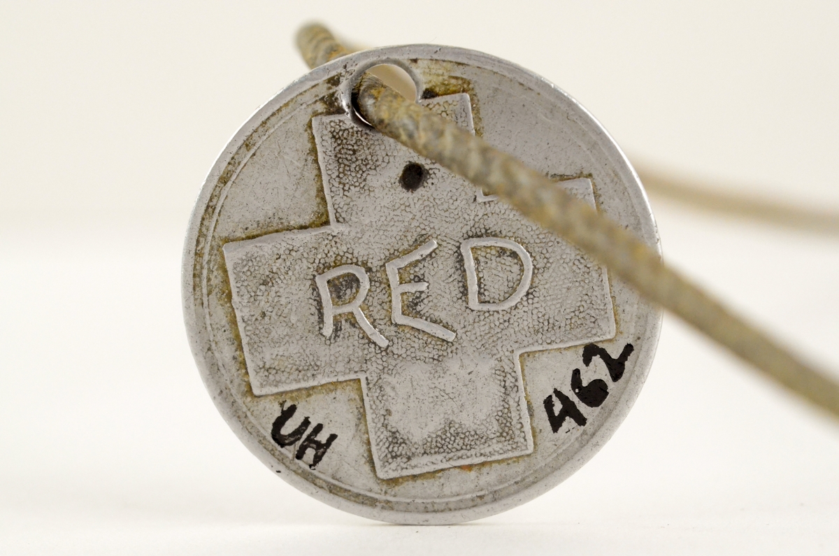 Dødsmerke. Metallplate, rund, flat, tredd inn på en tvunnet snor. På den ene siden et kors med bokstavene RED. På den andre siden: Co. H 1st. Infantry Montana 55, US. Vol.