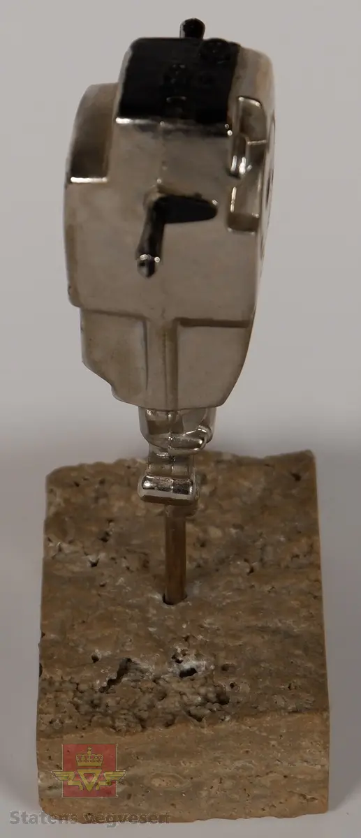 COBRA. Sølvfarget miniatyr boremaskin i metall som står med boret festet i en sokkel av stein. Boremaskinen har innskriften COBRA, og på steinsokkelen er det et klistremerke som har påskriften COBRA 148/248.
