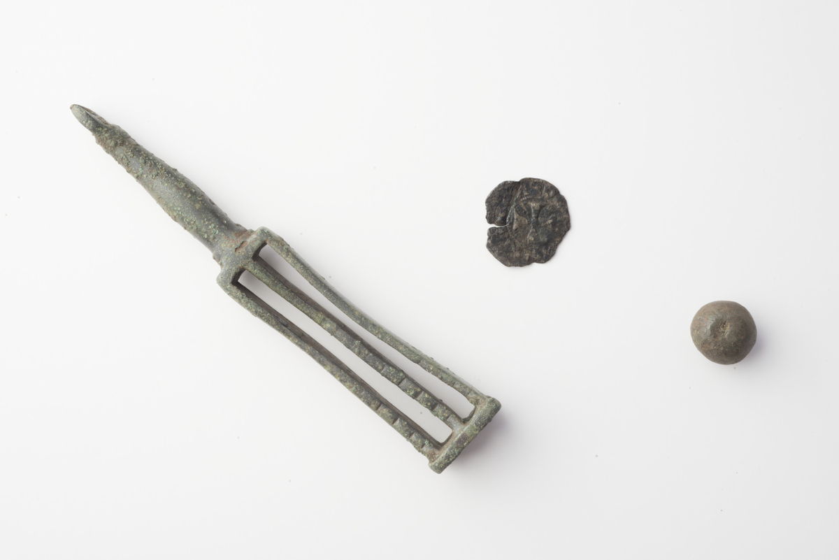 Mynt av sølv med høyt innhold av kobber, Norge, Magnus Lagabøte (1263-1280). Mynten er sterkt korrodert og med knekte og sprukne kanter. Adversen er svært utydelig mens på reversen er et kors synlig i midtfeltet identisk med Skaare fig. 215. Bokstavene som omgir korset er svært utydelige.