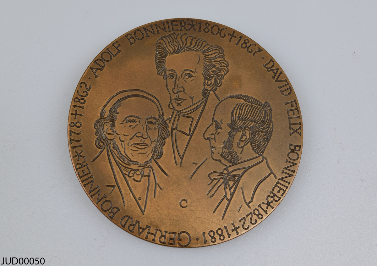 Två stycken bronsmedaljer med olika personer ur familjen Bonnier i profil på ena sidan, samt graverade ansikten på andra sidan.