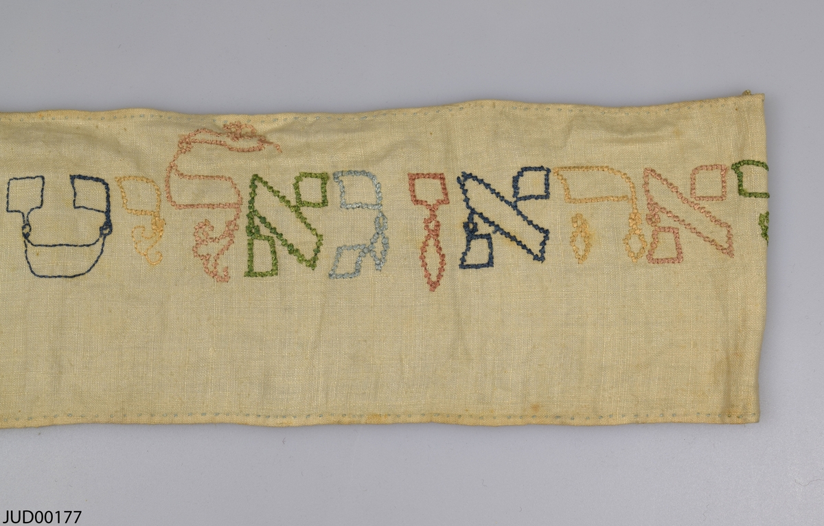 Torabindel (wimpel) tillverkad av linne, som är dekorerad med broderi i olika färger i form av hebreisk text och året 1677.